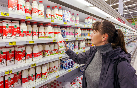 年轻女子选择新鲜的牛奶生产在购物在乳品苏