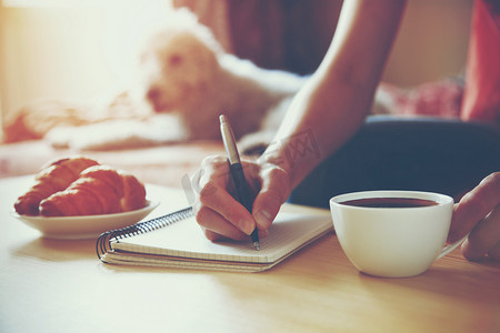 用笔写上笔记本与早晨喝咖啡的女性手