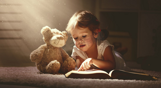 魔法故事摄影照片_孩子读一本魔法书在黑暗的家中的小女孩 