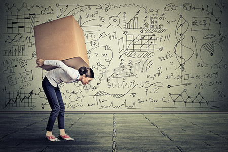 woman carrying heavy box walking along gray wall 