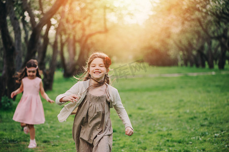 在春天的花园中运行的两个快乐小女友。姐妹花时间在一起的孩子户外和玩。季节性活动上行走