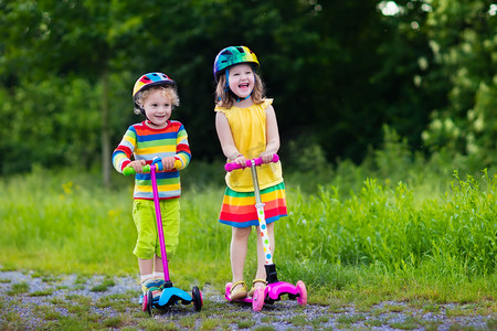 彩虹朋友摄影照片_孩子们骑着滑板车中夏公园