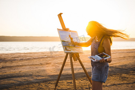 年轻女子艺术家画风景画在露天沙滩上