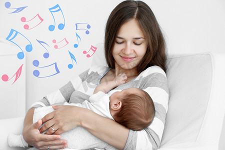 母亲用熟睡的婴儿坐在扶手椅上。摇篮曲歌曲和音乐概念