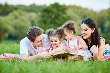 火爆预定摄影照片_年轻家庭阅读一本书在户外躺在草丛中，p