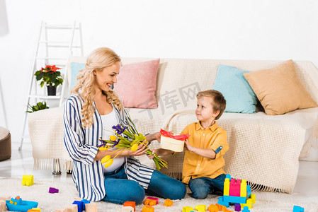 小男孩呈现微笑怀孕的母亲郁金香花和心形礼品盒