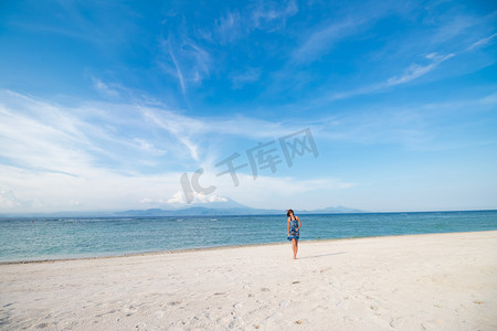 穿着蓝色衣服的热带小岛的海滩上行走印度尼西亚努沙蓝梦的年轻女人。令人惊异的天空，海景。阿贡火山和岛屿巴厘岛的背景.