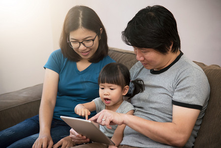 年轻亚洲家庭摄影照片_亚洲家庭坐和玩数字平板的幸福.