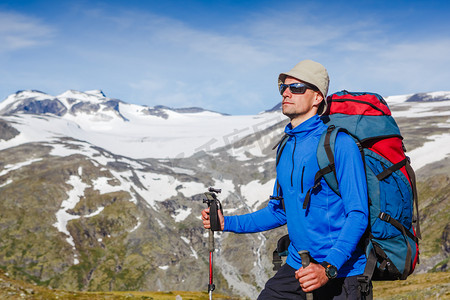 登山运动背景摄影照片_徒步旅行者看着山景的背包徒步旅行。挪威景观