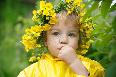 一个穿着黄色雨衣的小孩子和一个毛茛的花圈从灌木丛中吃浆果。.