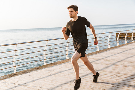 英俊的年轻运动员在沙滩上奔跑的形象听音乐用耳机.