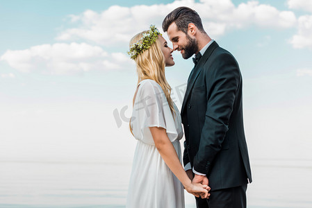 两人牵手摄影照片_婚礼情侣西装和白色礼服牵手, 触摸与鼻子在海滩上