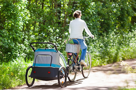 母亲在自行车与婴儿自行车拖车在公园
