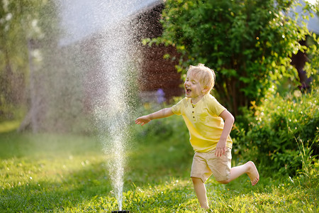 在阳光明媚的后院玩花园洒水车的滑稽小男孩。学前儿童玩喷雾水的乐趣。儿童夏季户外活动.