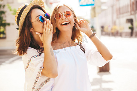 时尚肖像的两个年轻时尚的嬉皮黑发和金发女郎在夏季晴朗的一天, 白色时髦的衣服摆在街头背景。模型共享秘密, 八卦.