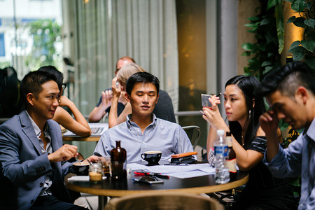 商务因为摄影照片_ 一群年轻精力充沛的亚裔同事围坐在桌旁, 进行着轻松的商务讨论。他们一边笑一边笑, 因为他们说话和交谈。.