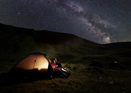 男人和女人在晚上休息, 在 Dogyaska 湖附近的喀尔巴阡山山露营, 坐在帐篷里, 看着布满星星的天空。在帐篷灯上.
