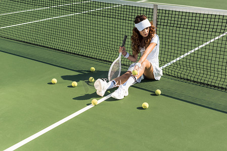 漂亮的女子网球运动员与球拍坐在网球网附近网球场周围球