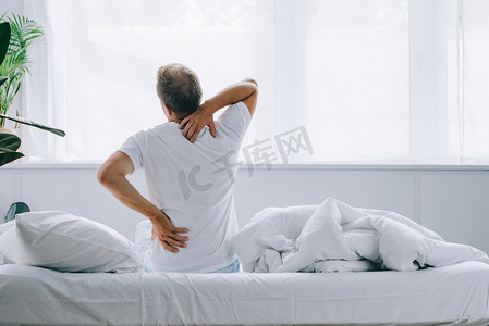 受苦摄影照片_坐在床上的人的背面和痛苦的背部疼痛