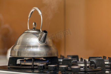 不锈钢背景摄影照片_闪亮的不锈钢茶壶茶壶与开水在煤气炉上的厨房黄色复制空间背景.