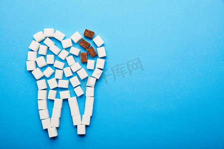 巧克力蛀牙摄影照片_白色和红糖立方体的顶视图排列在牙标志在蓝色背景, 蛀牙概念