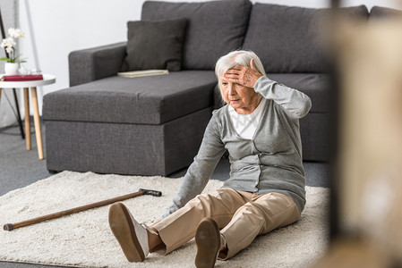 老年妇女偏头痛坐在地毯上，用手触摸额头