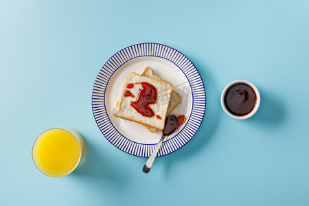 橙汁、烤面包、碗和勺子的顶视图，在蓝色背景的装饰板上加果酱