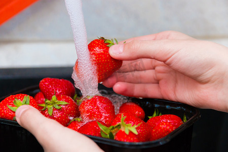 洗一洗摄影照片_在洗草莓。女孩在一股浓密的水流下冲洗成熟的草莓，在吃之前彻底洗净草莓。有选择的重点.