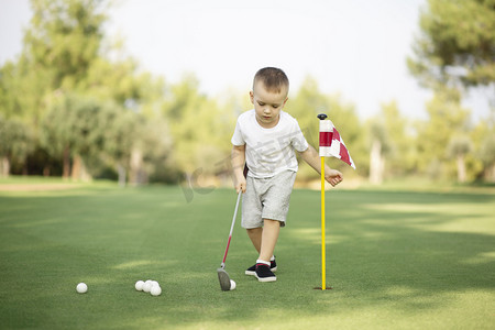 推杆摄影照片_小男孩打高尔夫，在绿草上推杆打球.