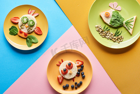 蓝色、黄色和粉红色背景上由食物制成的花哨动物的盘子的顶视图