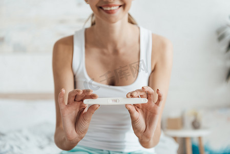 微笑的年轻女子显示怀孕测试的局部视图 