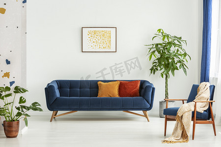 中世纪现代椅子与毯子和一个大沙发与五颜六色的垫子在一个宽敞的客厅内部与绿色植物和白色墙壁。真实照片.