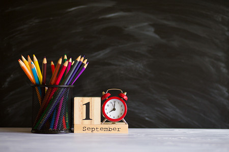 观念回到学校。重新闹钟与彩色铅笔和木制日历设置在9月1日黑色黑板背景。设计复制空间用品