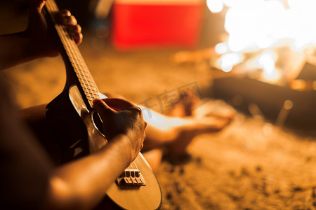 海滩上的篝火旁, 一位音乐人在弹几弦琴吉他.