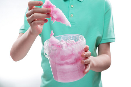 裁剪拍摄的孩子拿着粉红色的棉花糖在塑料桶
