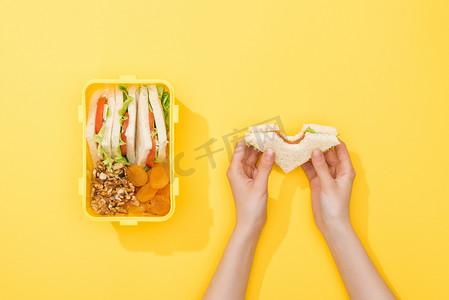 裁剪视图的妇女持有三明治附近的午餐盒与坚果，干杏和小吃
