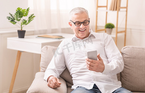 快乐的老人坐在沙发上用智能手机