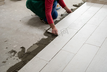 在新公寓的建筑工地上安装陶瓷砖的熟练工人在地板上制造层压板地板