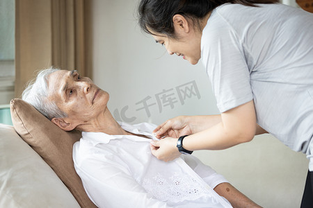 女性身体摄影照片_照顾老人的亚洲女性护理人员，为瘫痪人士、四肢瘫痪、身体或肌肉无力的年长女性提供衣物、钮扣或更衣服务