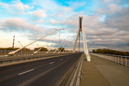 高速公路穿过一座有钢丝绳的斜拉桥，在夕阳西下，在蓝天和云彩的映衬下进行特写
