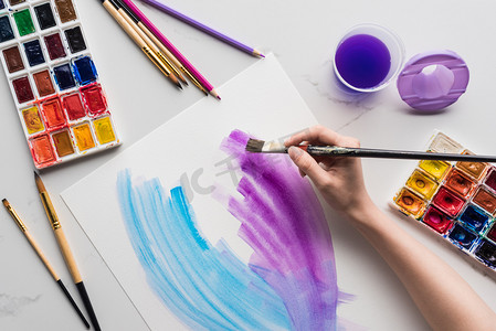 艺术家在大理石白色表面上的白纸上绘制紫色和蓝色水彩笔触的裁剪视图