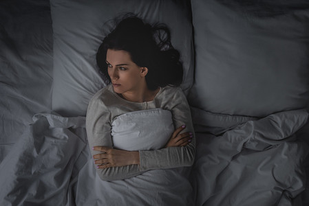睡眠障碍和交叉双臂躺在卧室的妇女的头像 