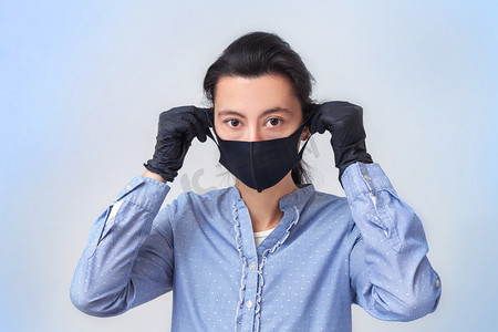 戴手套的女孩戴上医疗面具.预防普通感冒和流感的病毒性疾病。浅灰蓝色背景。戴着呼吸面具.