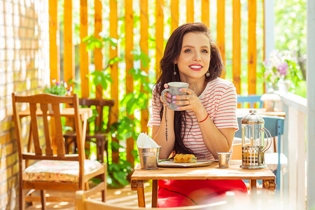 种植园主摄影照片_微笑的女人在咖啡馆的露台上喝咖啡.