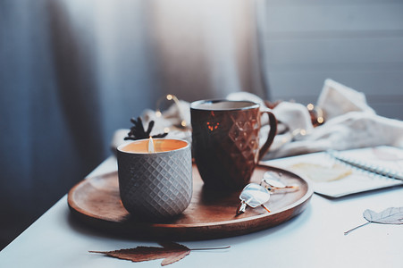 舒适的秋天或冬天的早晨在家。静止不动的生活细节与一杯茶，蜡烛，素描书与水族馆和温暖的毛衣。斯堪的纳维亚海格概念