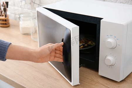 Woman opening modern microwave oven in kitchen