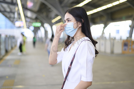 pandemic摄影照片_一名年轻女子站在地铁站站台上，戴着口罩，保护Covid-19，这是新的正常旅行理念.
