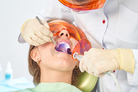 Girl child at the doctor. Dentist places a filling on a tooth with dental polymerization lamp in oral cavity. over clinic background