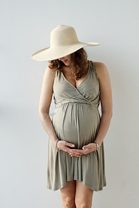 那个戴帽子抱着大肚子的无亲昵的孕妇的近照。在等孩子。母性.