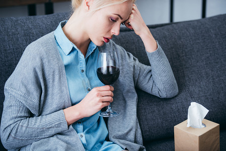 心烦意乱的女人坐在家里喝了一杯红酒和纸巾盒